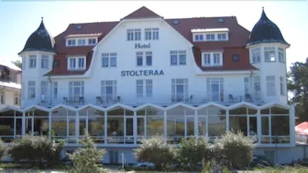 A hotel named 'Hotel Stolteraa' with a large building, a sandy beach, and people relaxing on the beach and in the water. - Hotel Stolteraa (Rostock)