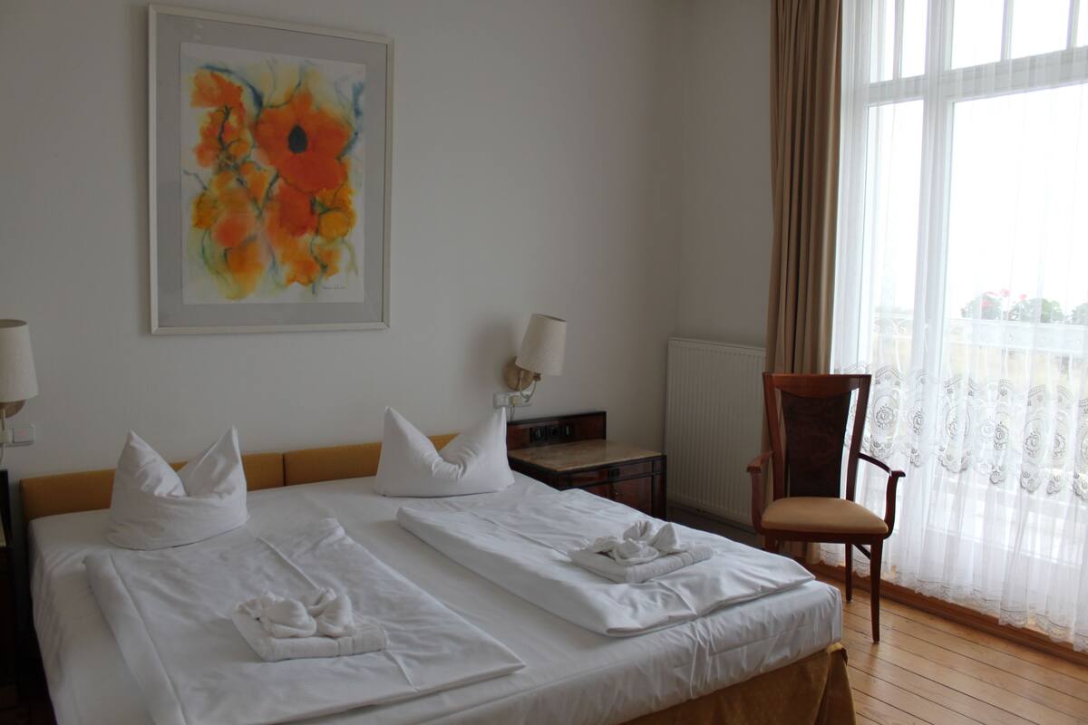 A hotel room with two beds, a painting on the wall, a chair, and a window with curtains.