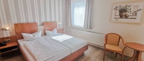 Ein Hotelzimmer mit einem großen Bett, einem Nachttisch mit Lampe, einem Sessel, einem kleinen Tisch und einem Fenster mit Vorhängen.