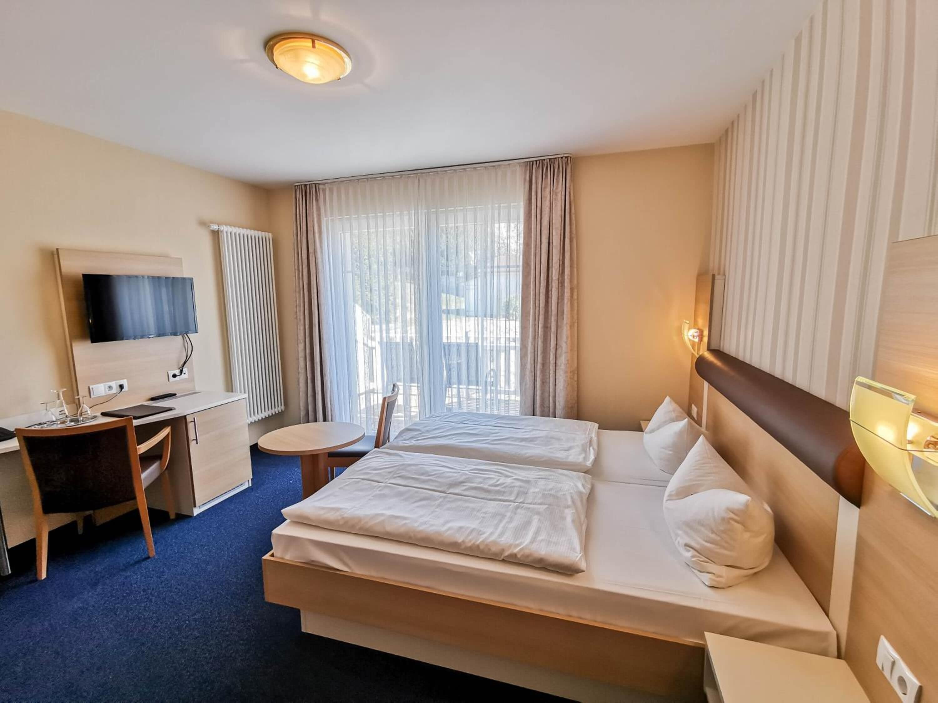 Een hotelkamer met een bed, een bureau, een stoel, een televisie en een raam met gordijnen.