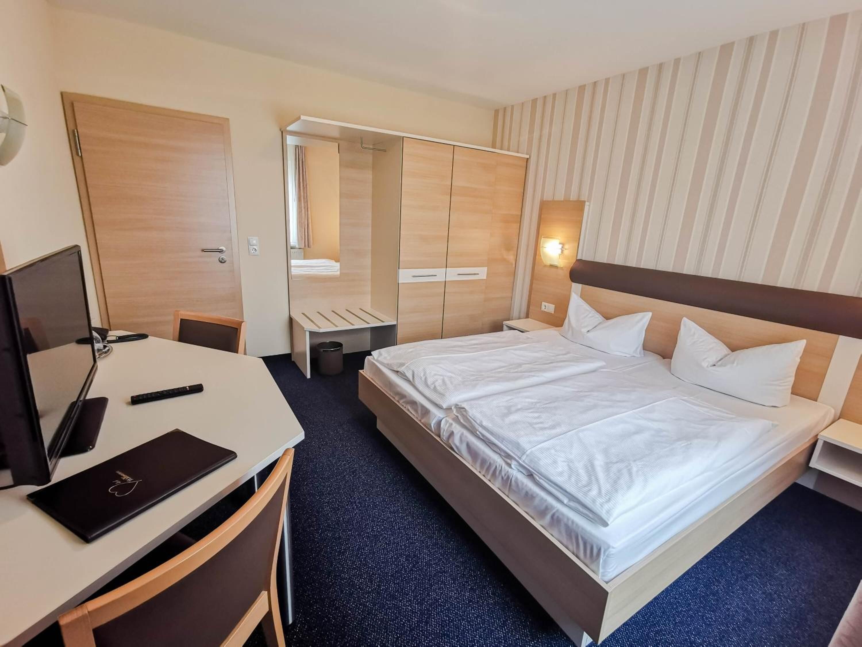 Ein Hotelzimmer mit Bett, Schreibtisch, Stuhl und Spiegel.
