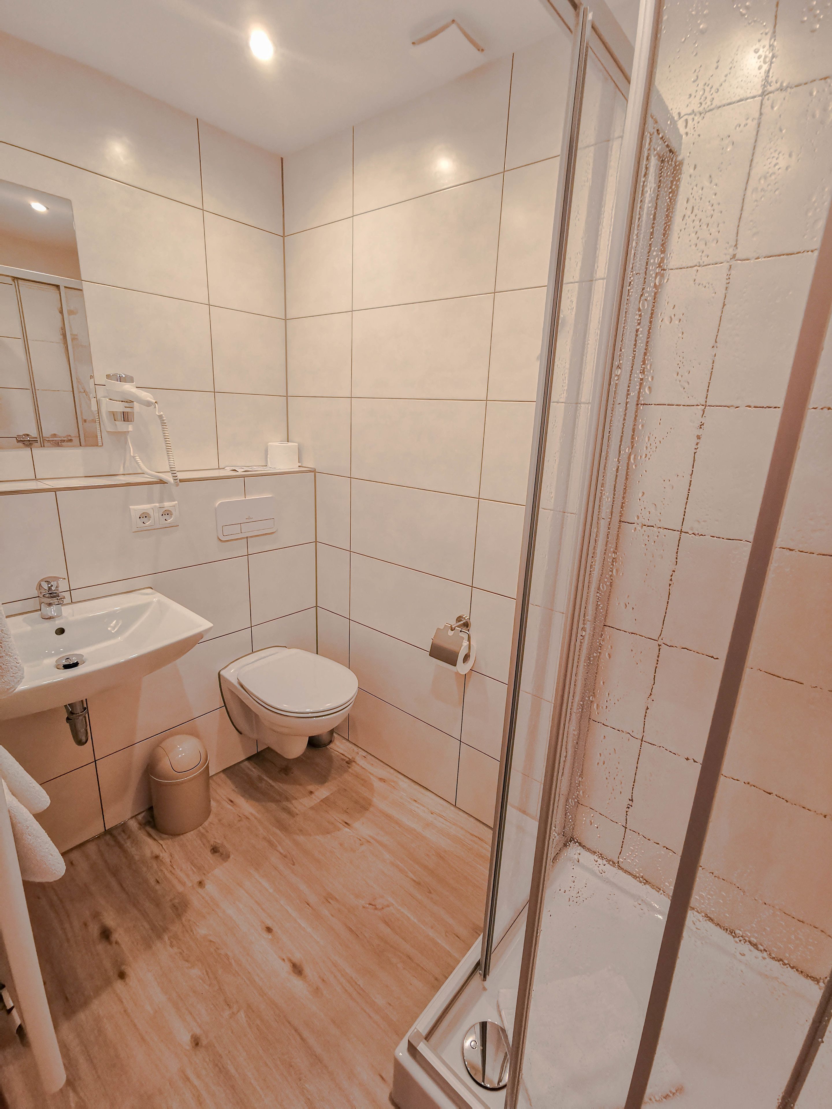 Un baño moderno con ducha, lavamanos, inodoro y espejo.