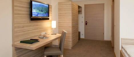 Una habitación de hotel con un escritorio de madera, una silla, un televisor montado en la pared y una cama.