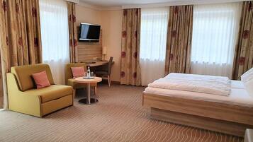 A hotel room with a bed, a sofa, a small table, a TV, and curtains.