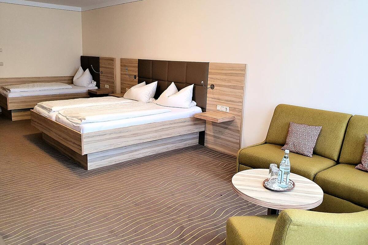 A hotel room with two single beds, a sofa, and a small round table with a decorative item.
