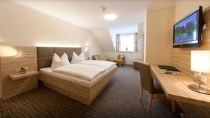 A hotel room with a large bed, a desk, a chair, a TV, and a window with curtains. - Hotel Strasshof (Pfaffenhofen an der Ilm)
