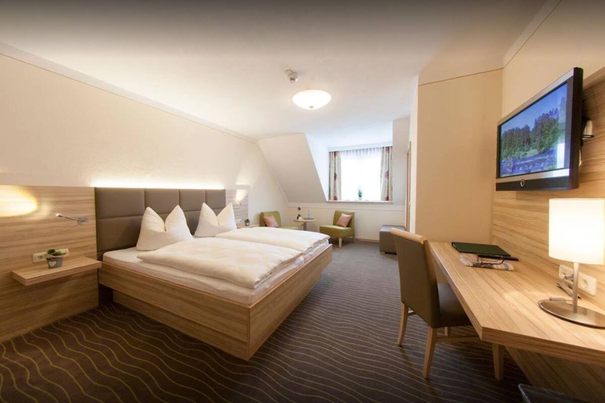 A hotel room with a large bed, a desk, a chair, a TV, and a window with curtains.