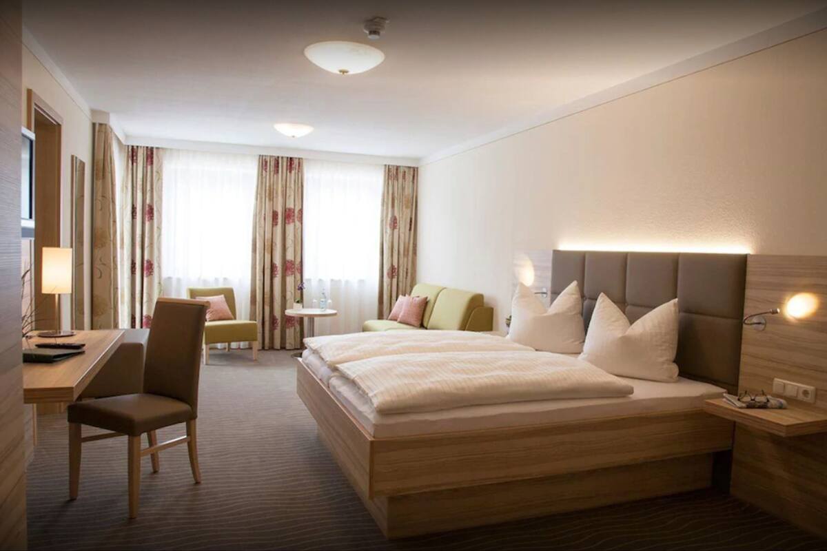 A hotel room with a large bed, a desk, a chair, and a small table.