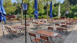 An outdoor seating area with tables and chairs, blue umbrellas, and a signpost. - Hotel Strasshof (Pfaffenhofen an der Ilm)