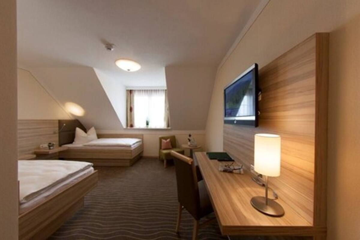 A hotel room with two single beds, a desk with a lamp, a television mounted on the wall, and a window with curtains.
