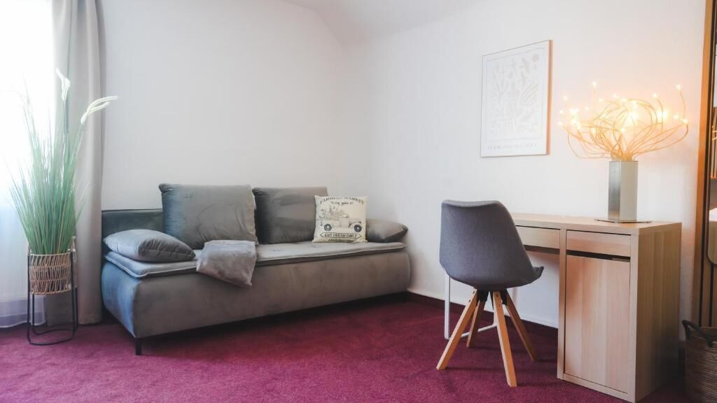 A modern living room with a sofa, a desk, a chair, a potted plant, and a wall-mounted lamp.