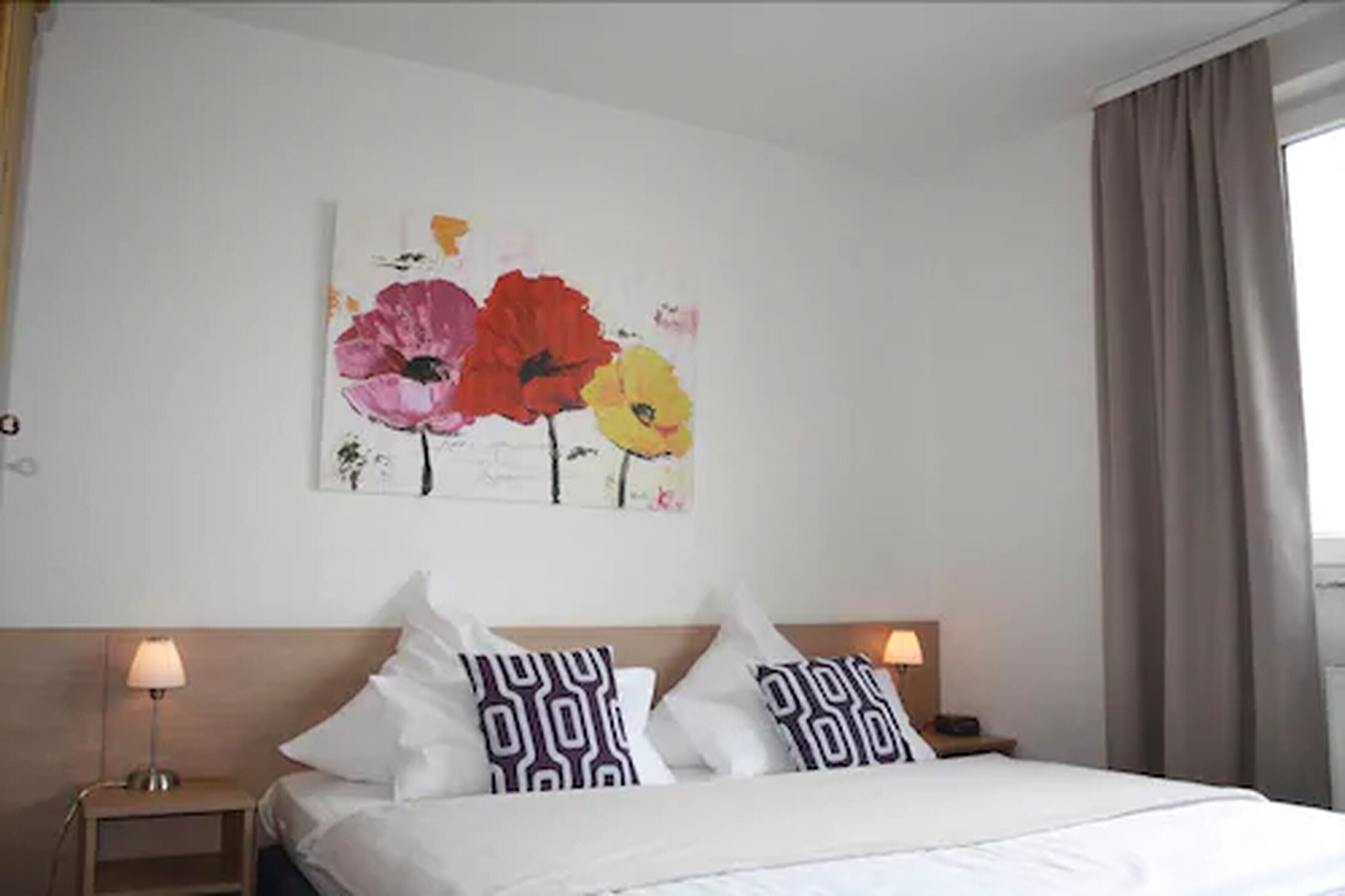 A hotel room with a bed, two bedside tables, and a wall-mounted painting of flowers.