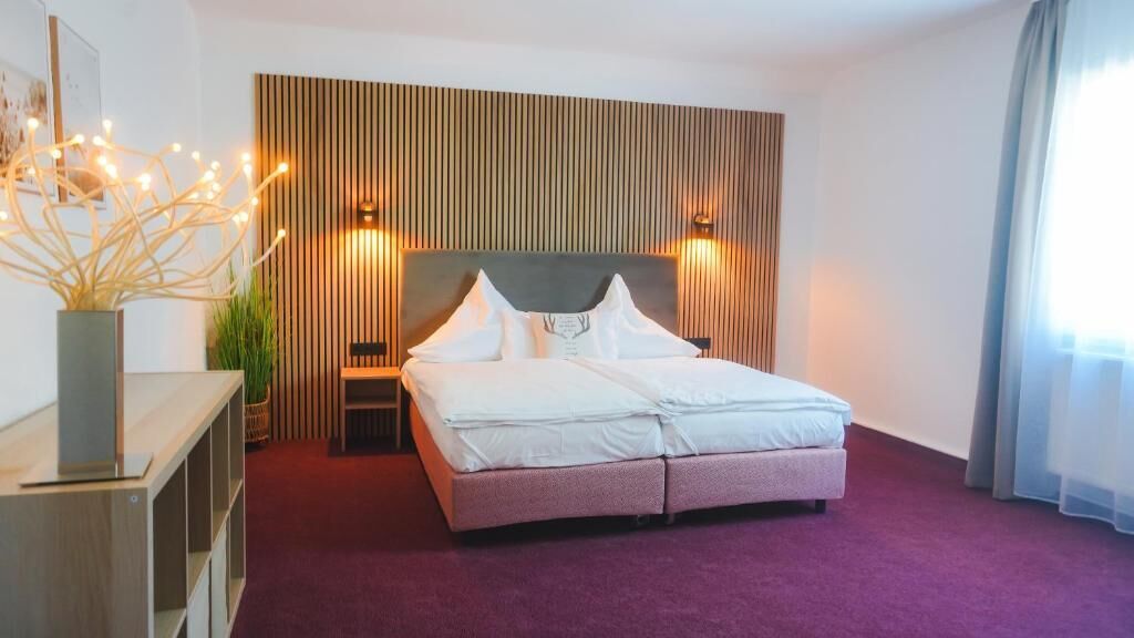 A hotel room with a large bed, a wooden headboard, two bedside lamps, and a nightstand.