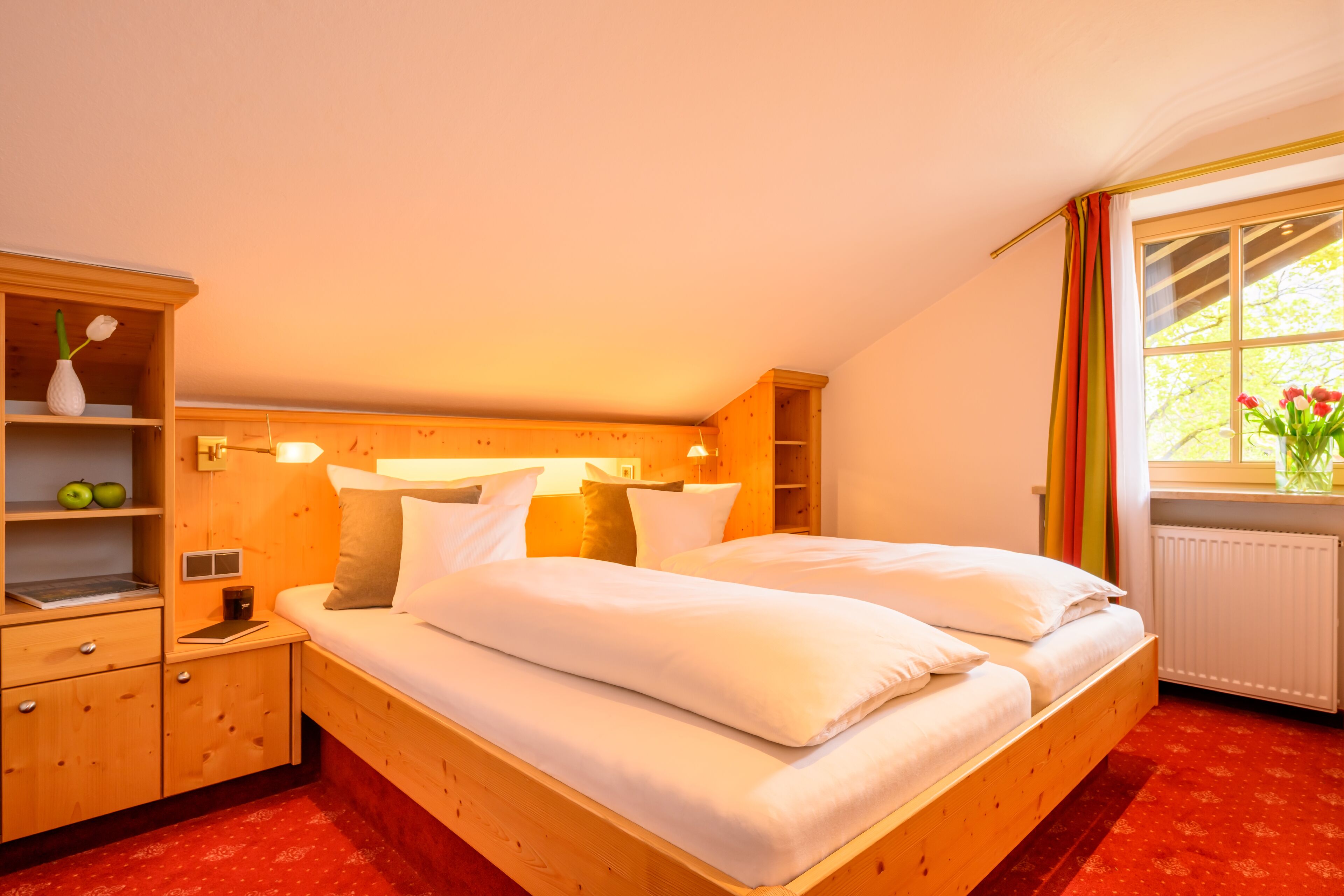 A bedroom with a wooden bed, a nightstand, a shelf with apples, and a window with curtains.