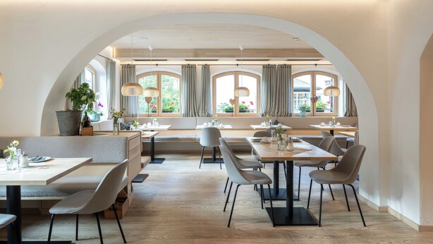A modern dining area with high tables and chairs, large windows with curtains, and a view of the outdoors. - Hotel Weinklause (Oberstdorf)