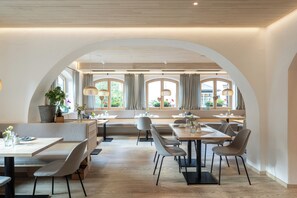 Un espace de restauration moderne avec des tables et des chaises hautes, de grandes fenêtres avec des rideaux et une vue sur l’extérieur.