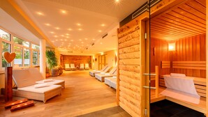 A spa area with wooden walls, a large window, and a seating area with cushions. - Hotel Weinklause (Oberstdorf)