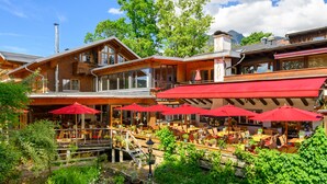 A restaurant with outdoor seating, red umbrellas, and a view of mountains. - Hotel Weinklause (Oberstdorf)