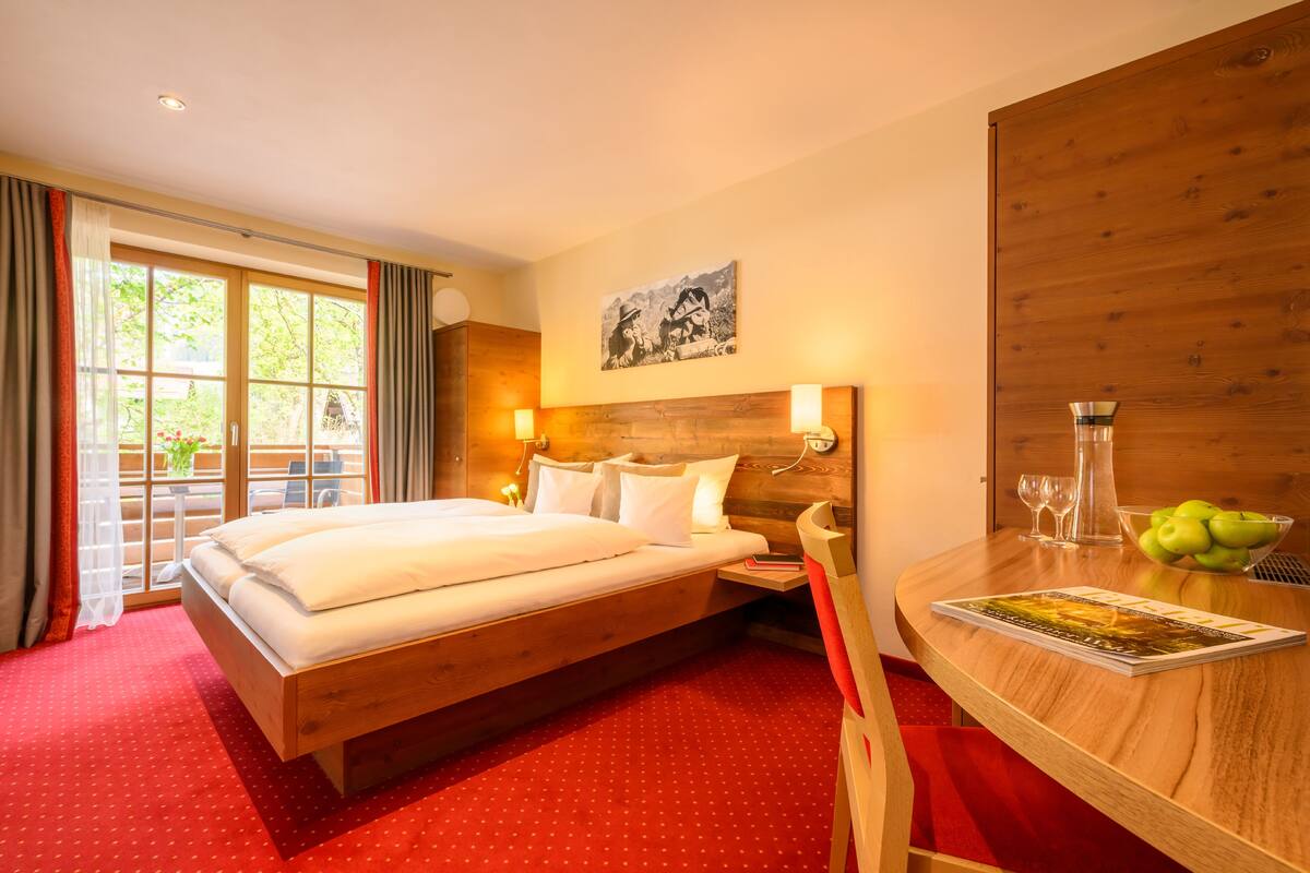 Camera d'albergo con un letto grande, una testiera in legno, un comodino con una ciotola di frutta, una rivista e un quadro appeso al muro.