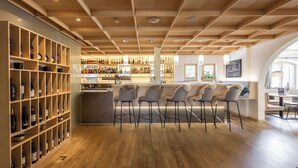A bar area with wooden shelves, bar stools, and a counter. - Hotel Weinklause (Oberstdorf)