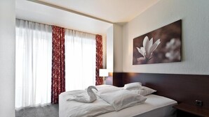 Een hotelkamer met een groot bed, hoofdeinde, een schilderij aan de muur en een raam met gordijnen.