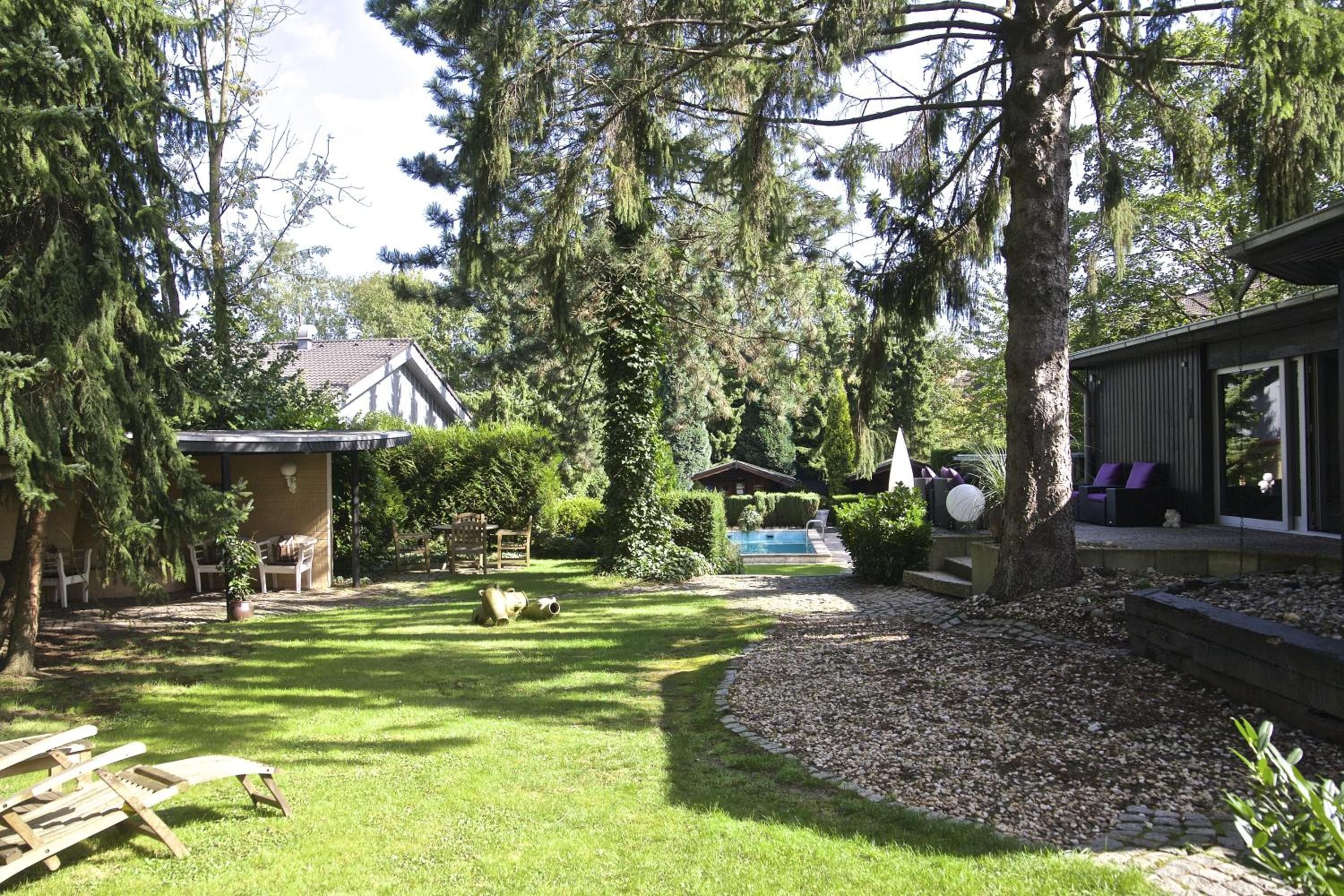 Ein Garten mit Schwimmbad, überdachter Terrasse und kleiner Gartenhütte.