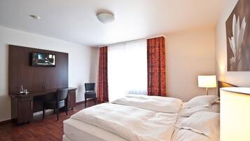 Habitación de hotel con cama, escritorio, silla, televisor y cortinas.
