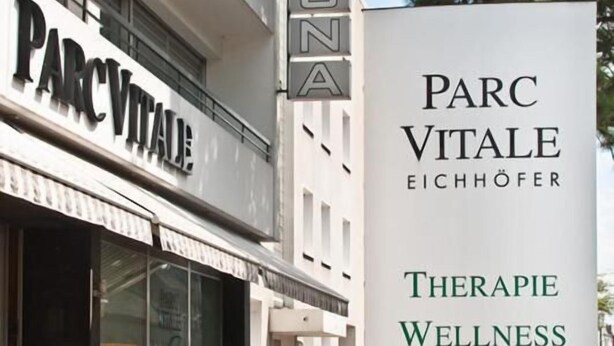 Een gebouw met een bordje 'PARC VITALE EICHHÖFER' en een overzicht van diensten, waaronder therapie, wellness, massage en sportgeneeskunde.