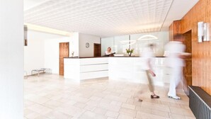 Een moderne receptie met een houten receptiebalie, een grote spiegel en een betegelde vloer.