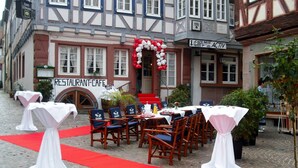 An outdoor restaurant setup with tables and chairs, a red carpet, and a building with a sign that reads "RESTAURANT-CAFE". - Hotel Schwanen (Mosbach)