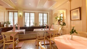 A dining area with white tables and chairs, a bench, and a wall-mounted mirror. - Hotel Schwanen (Mosbach)