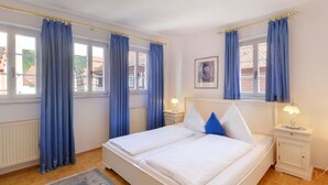 A hotel room with a double bed, two bedside tables with lamps, a framed picture on the wall, and large windows with blue curtains. - Hotel Schwanen (Mosbach)