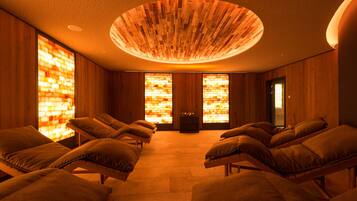 A room with wooden walls and a ceiling with a circular wooden design. There are multiple massage chairs with cushions.