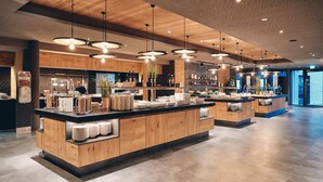 A modern kitchen area with wooden cabinets, a central island with a black countertop, and pendant lighting.