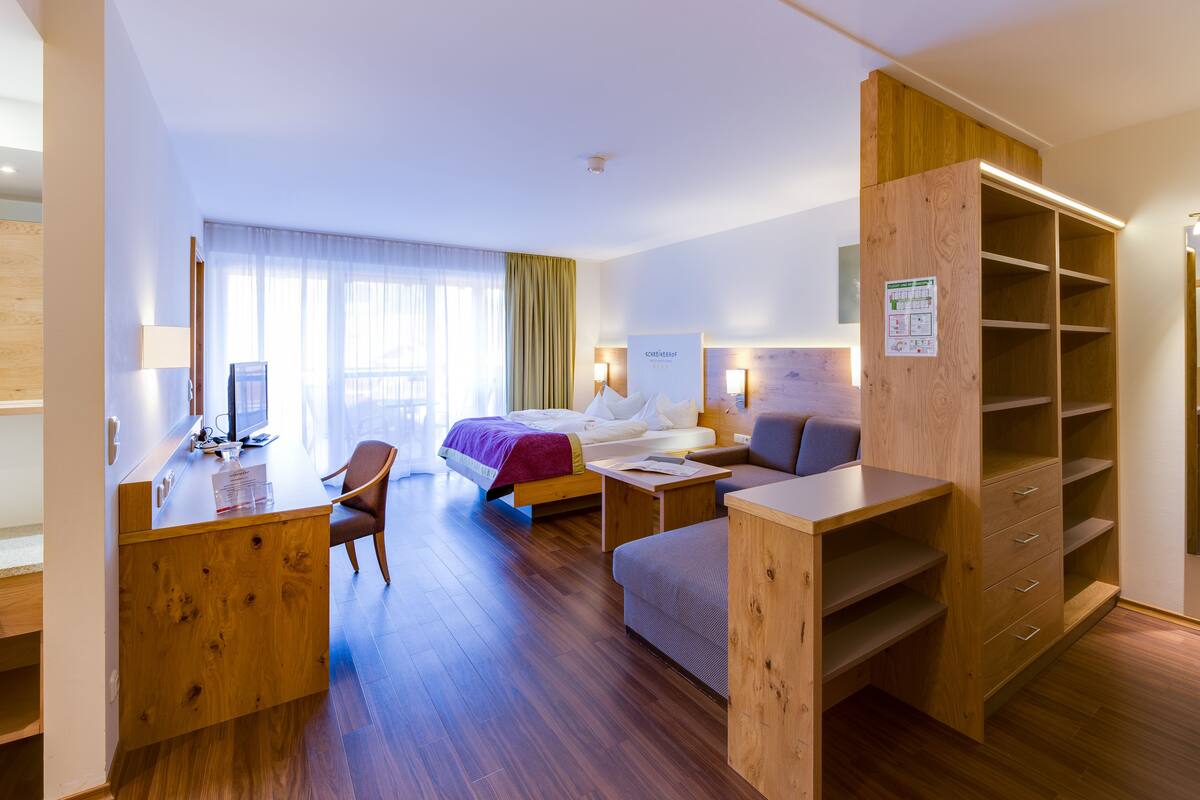 Une chambre d’hôtel comprenant un lit, un bureau, une chaise et une étagère en bois.