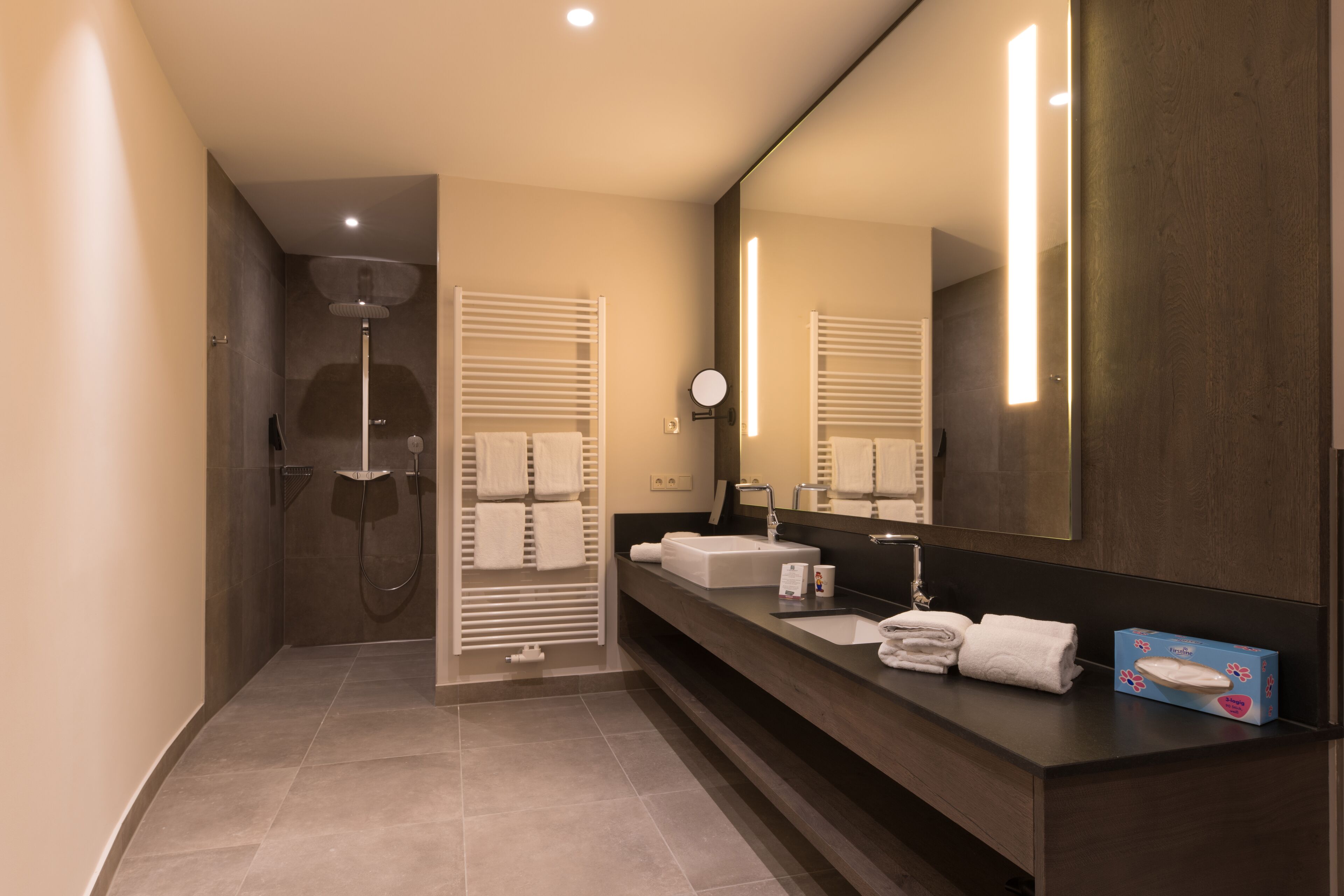 Een moderne badkamer met een grote spiegel, twee wasbakken, een douche en een handdoekrek.