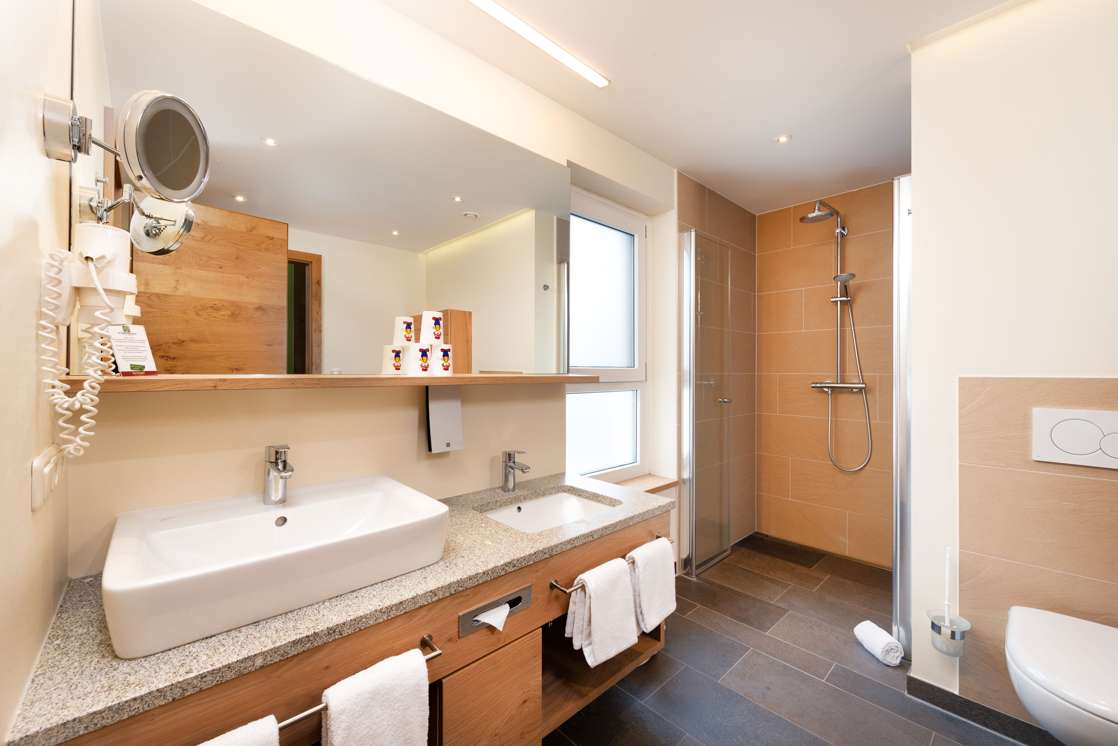 A modern bathroom with a large mirror, two sinks, a shower, and a toilet.