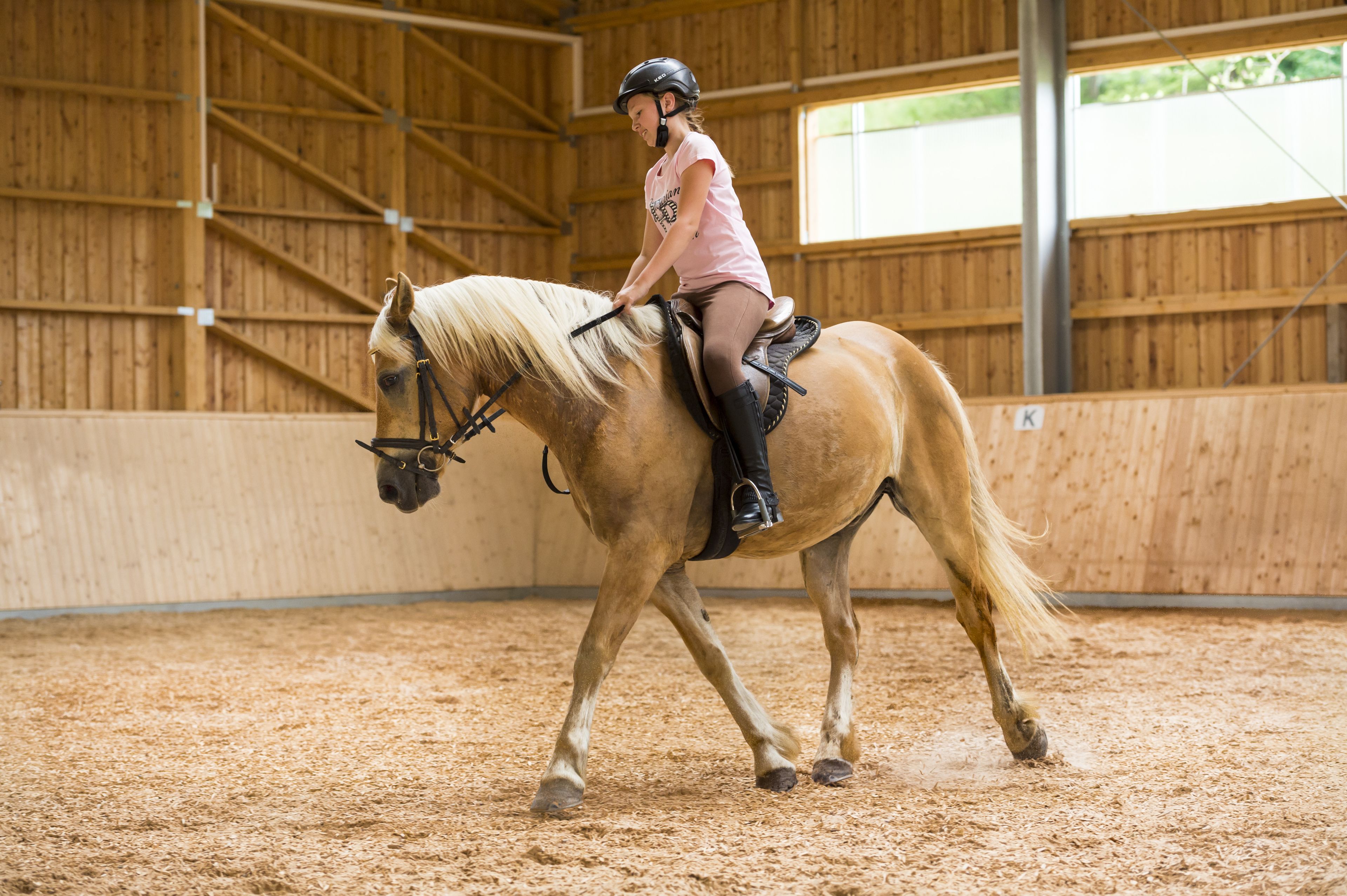A person riding a horse inside a stable with wooden walls and a sandy floor.