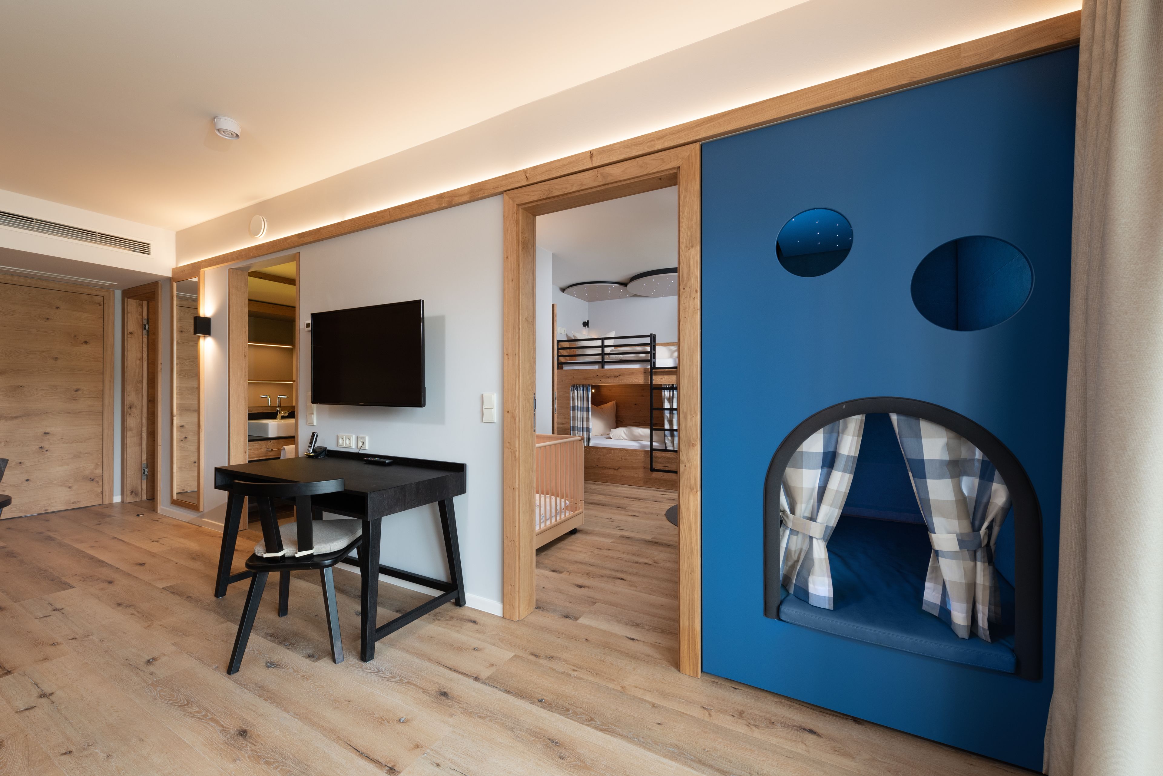 A modern interior with a wooden floor, a dining area with a table and chairs, a bunk bed, and a blue play area with circular cutouts.
