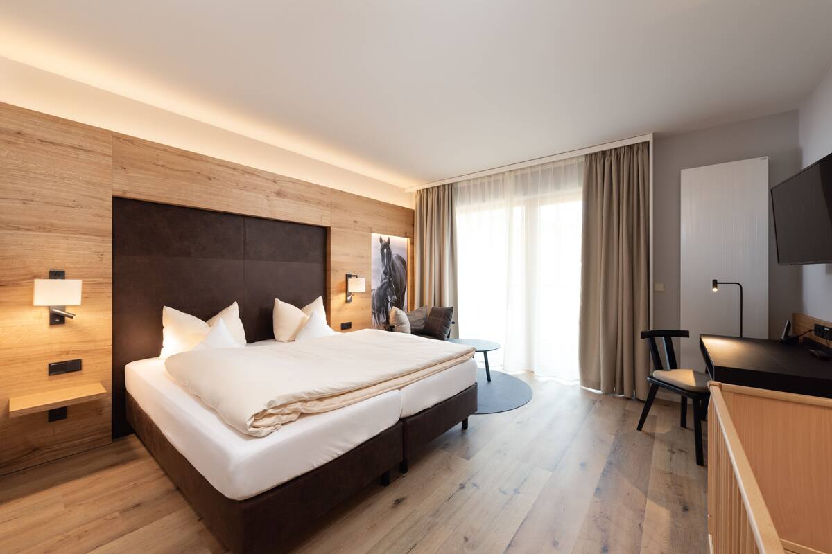 Une chambre d’hôtel moderne avec un grand lit, des murs lambrissés en bois, un bureau et une télévision.