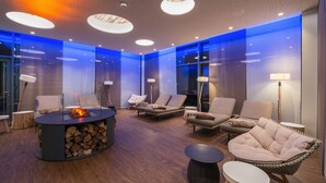 A modern lounge area with a central fire feature, comfortable seating, and ambient lighting.