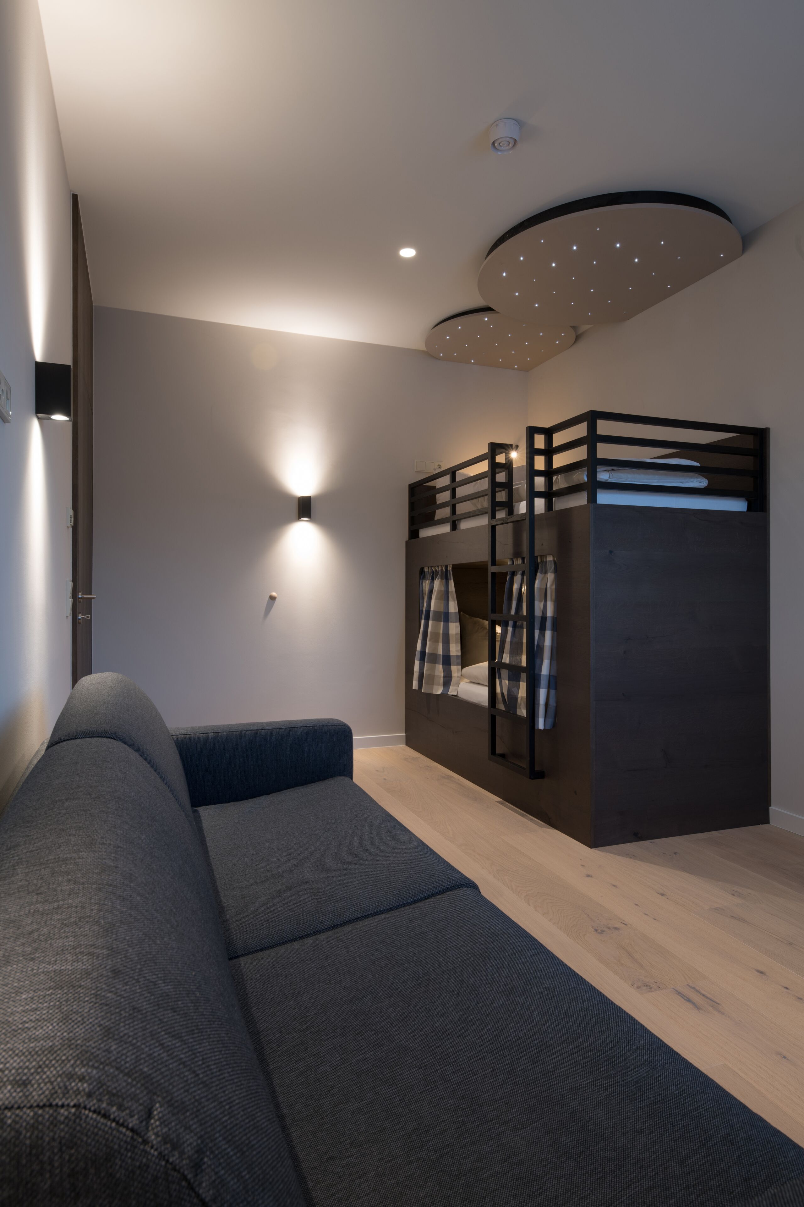 Een moderne kamer met een stapelbed, een slaapbank en een wandlamp.