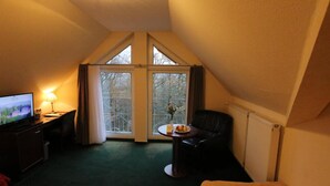 A small, triangular room with a television, a desk, a chair, and a table with a plate of food. - Panoramahotel Am Marienturm (Rudolstadt)
