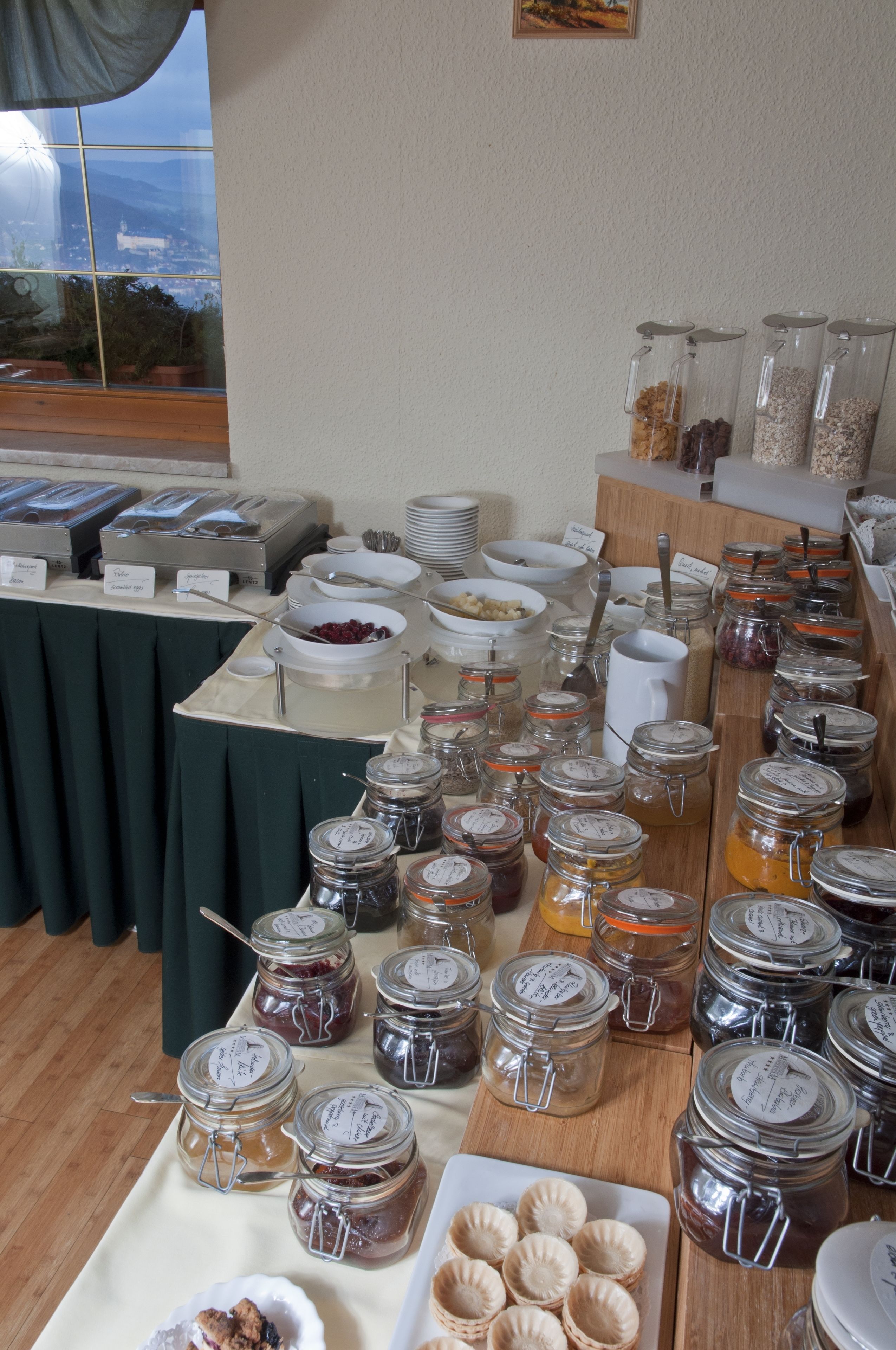 A buffet table with various food items and condiments, including jars of preserves and bowls of fruits.