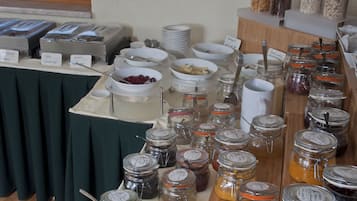 A buffet table with various food items and condiments, including jars of preserves and bowls of fruits.
