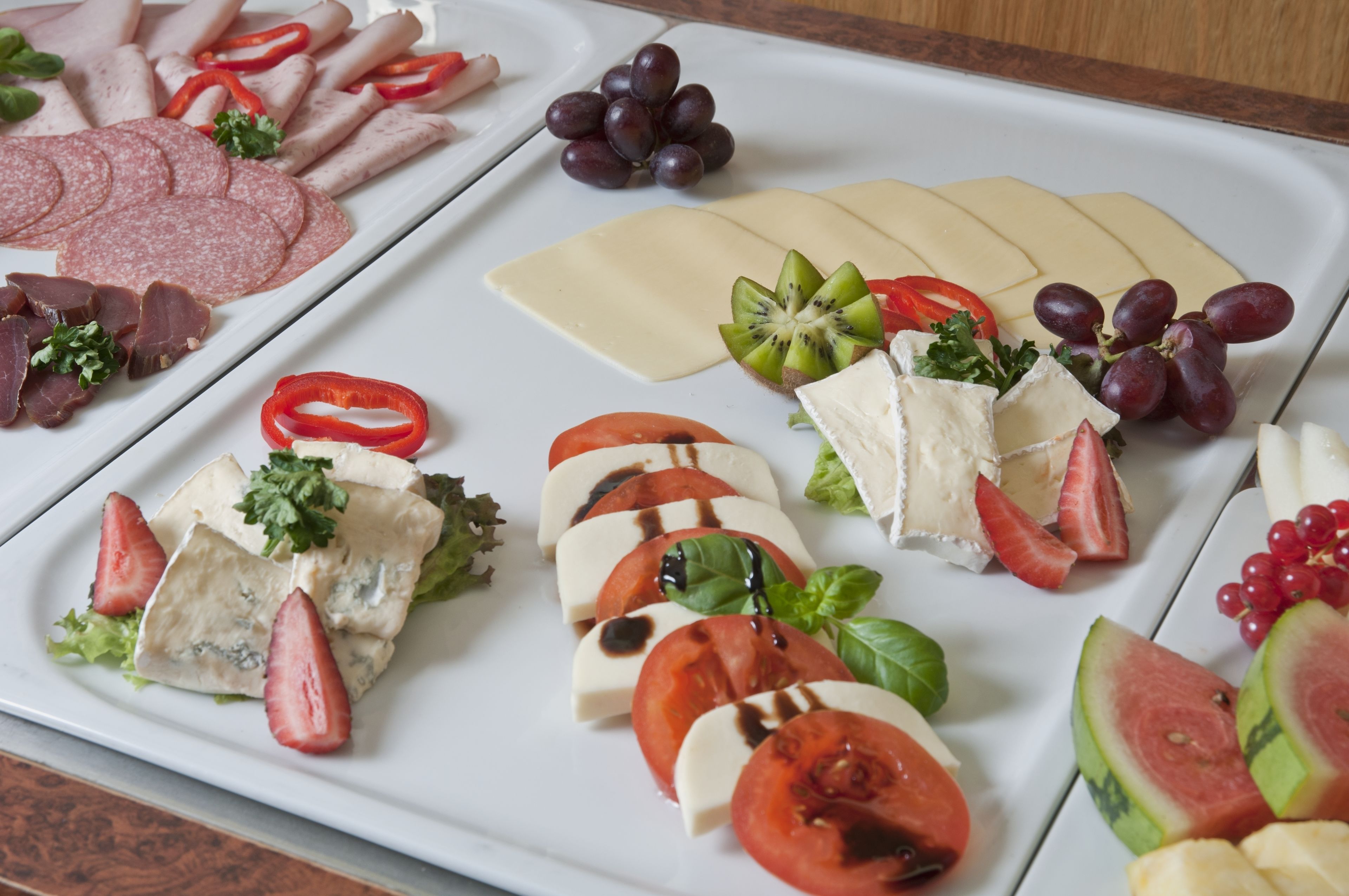 Eine Auswahl an Speisen, darunter Aufschnitt, Käse und Obst, an einem Tablett angerichtet.