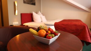 A hotel room with a bed, a red blanket, a white pillow, a fruit bowl on a table, and a wall-mounted light. - Panoramahotel Am Marienturm (Rudolstadt)