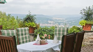 A table set for two with plaid cushions, a white tablecloth, and a view of a town and mountains in the background. - Panoramahotel Am Marienturm (Rudolstadt)
