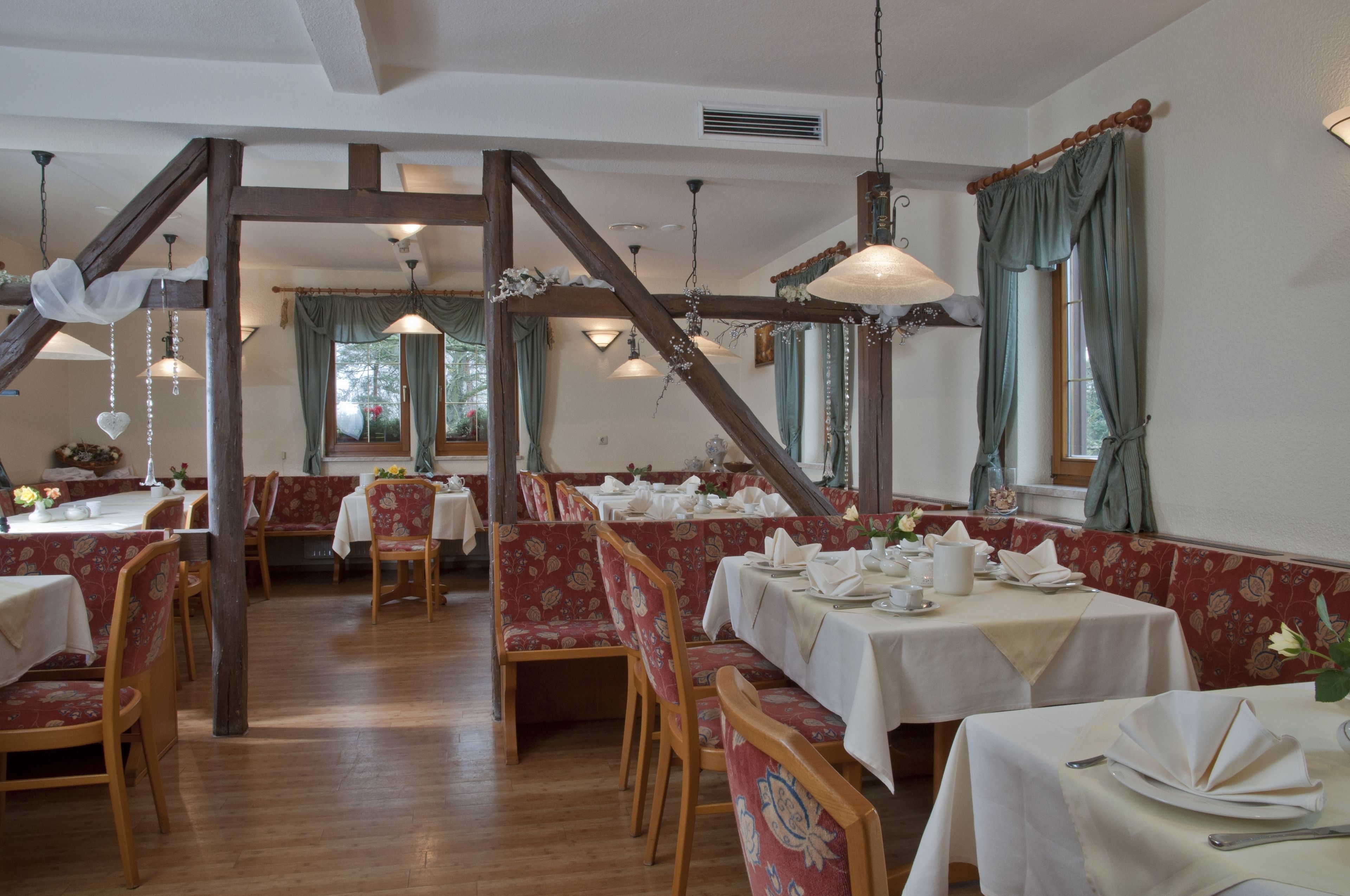 A dining area with wooden beams, red upholstered booths, and white tablecloths.