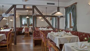 A dining area with wooden beams, red upholstered booths, and white tablecloths.
